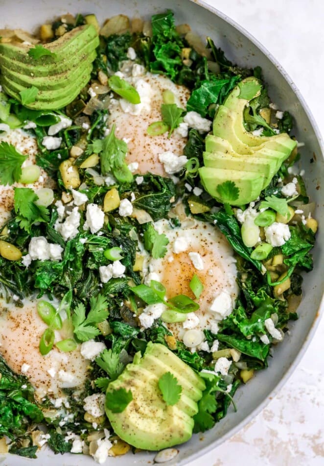 A closeup of the eggs cooking in the skillet with spinach, kale, zucchini, garlic and onions. It's been topped with feta cheese crumbles.