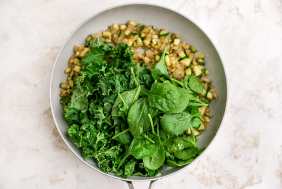 Chopped kale and spinach being added to the skillet.