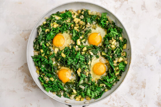 Four eggs cracked into a skillet containing kale, spinach, zucchini, onions, garlic and spices.