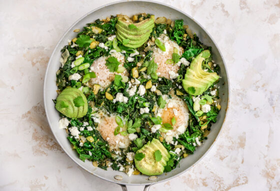The 4 eggs have cooked in the skillet with kale, spinach, zucchini, onion, garlic and spices. Slices of avocado have been added in 4 places evenly around the edges of the skillet.