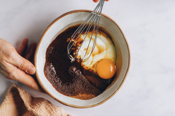 A mixing bowl with coconut oil, yogurt, coconut sugar, vanilla and egg being whisked together.