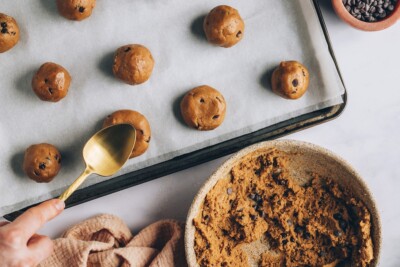 Balls of cookie dough being flattened with the back of a spoon on a baking sheet lined with parchment paper.