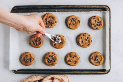 A spoon with additional chocolate chips to add more chocolate chips to the tops of the cookie dough that have been portioned out on a baking sheet.