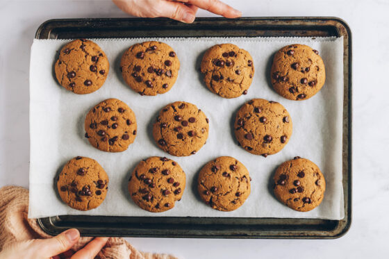Eleven freshly baked healthy chocolate chip cookies on a baking sheet lined in parchment paper.