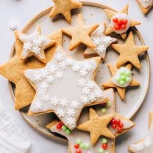 An overhead photo looking at a plate of healthy sugar cookies. Some of the cookies have been decorated with white icing and red, green or white sprinkles and some of the cookies are plain.