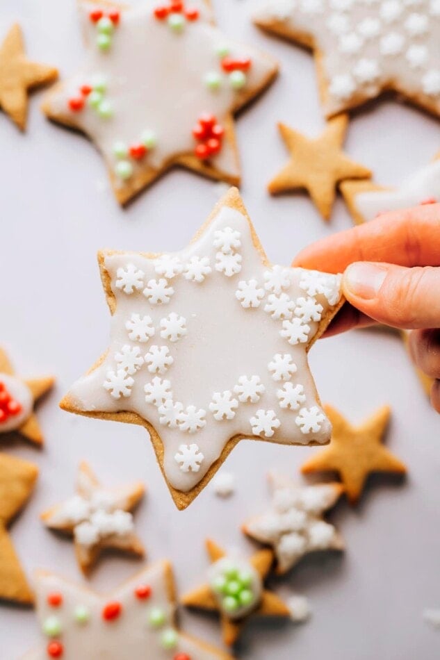 A hand holding up a star shaped healthy sugar cookie that has been decorated with white icing and white sprinkles.