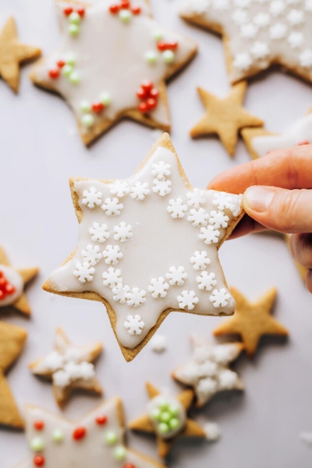 A hand holding up a star shaped healthy sugar cookie that has been decorated with white icing and white sprinkles.