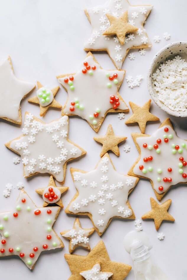 Various sized star shaped healthy sugar cookies scattered around a countertop. Some of the cookies have been decorated and some are plain.