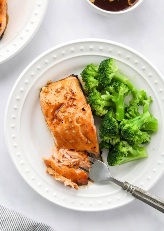 An overhead photo of a filet of maple glazed salmon and steamed broccoli on a plate. A fork is flaking off some of the salmon.