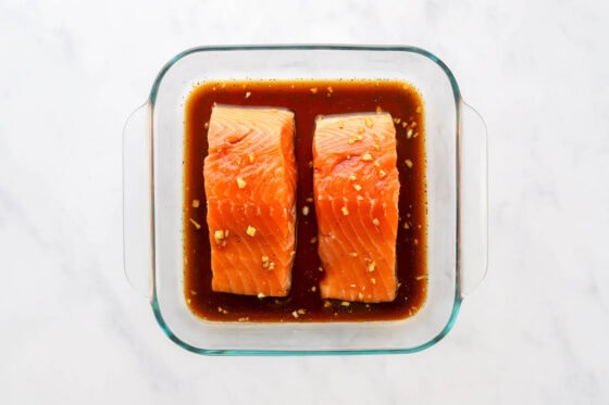 Two salmon filets marinating in a maple syrup, tamari, lemon juice, garlic, ginger and ground pepper mixture.