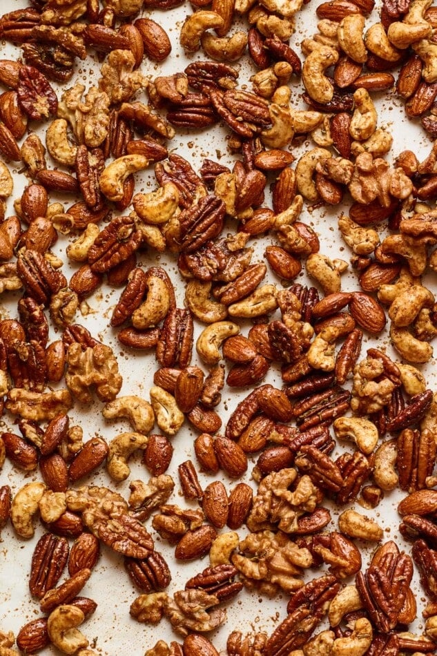 A close up of freshly baked sweet and savory party nuts on a parchment paper lined baking sheet.