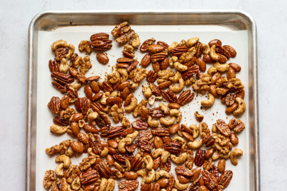 Sweet and savory party nuts spread on a baking sheet lined with parchment paper.