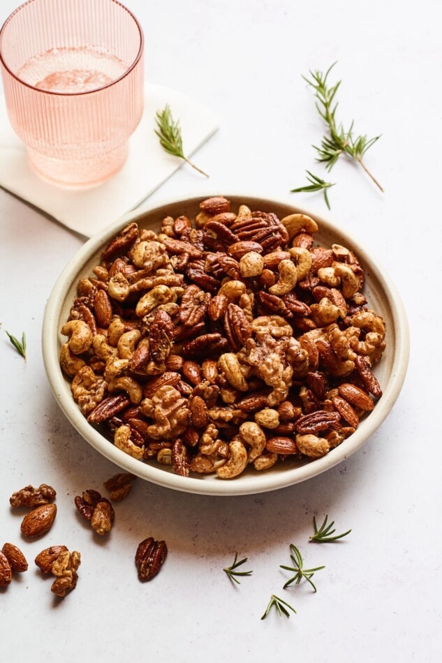 A bowl of sweet and savory party nuts next to a pink glass with water.