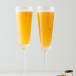 Two champagne flutes containing an easy peach Bellini.