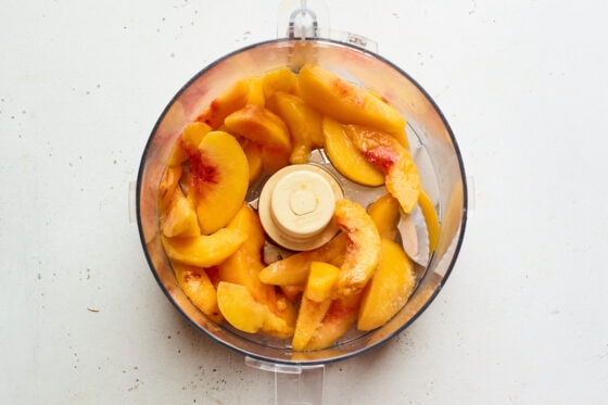 A food processor containing sliced peaches.
