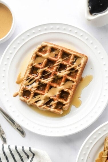 An overhead photo looking at a plate with a rectangular protein waffle that has been drizzled with maple syrup and peanut butter.