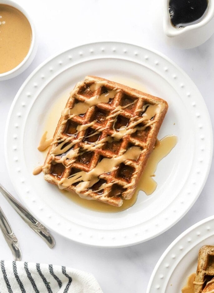 An overhead photo looking at a plate with a rectangular protein waffle that has been drizzled with maple syrup and peanut butter.