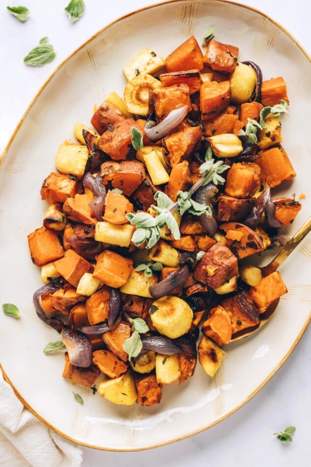Caramelized roasted root vegetables with sweet potatoes, carrots, parsnips and fresh oregano. Such an easy side for the holidays or everyday meals. An overhead photo of a serving dish with roasted root vegetables.