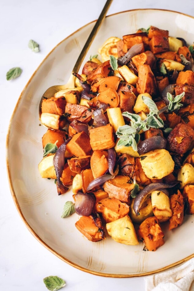 Caramelized roasted root vegetables with sweet potatoes, carrots, parsnips and fresh oregano. Such an easy side for the holidays or everyday meals. A platter of roasted root vegetables with a gold serving spoon.