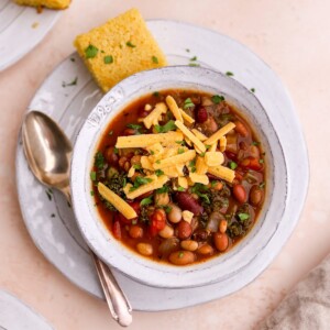 A bowl of 15 bean soup topped with a slice of corn bread, shredded cheese and fresh parsley.