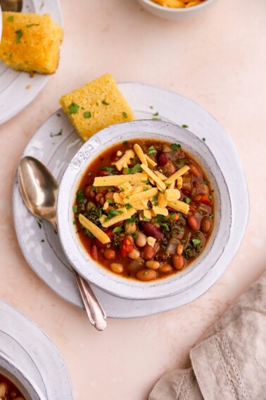 A bowl of 15 bean soup topped with a slice of corn bread, shredded cheese and fresh parsley.