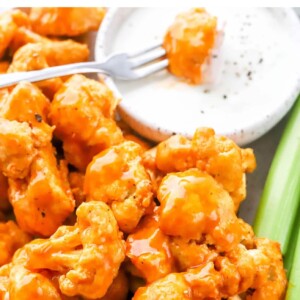 Plate of air fried buffalo cauliflower with ranch and celery. Fork has a buffalo cauliflower piece in the ranch.