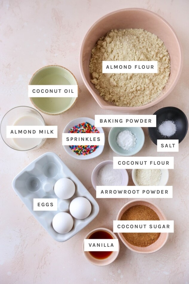 Ingredients measured out to make almond flour cupcakes: almond flour, coconut oil, baking powder, almond milk, sprinkles, salt, coconut flour, arrowroot powder, eggs, coconut sugar and vanilla.