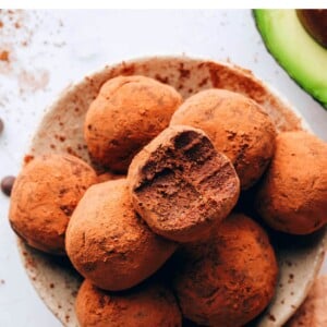 An overhead photo of a bowl of avocado truffles. The top truffle has a bite taken out of it.