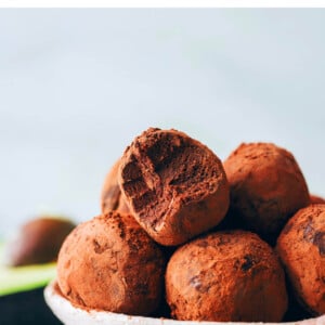 A bowl of chocolate avocado truffles. One of the truffles has a bite taken out of it.
