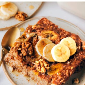 A serving of banana bread baked oatmeal on a plate topped with fresh banana slices and walnuts.