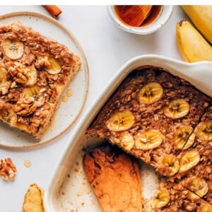 Banana Bread Baked Oatmeal in a baking dish. The oatmeal has been portioned in to 4 servings, with one serving removed from the baking dish and on a plate.