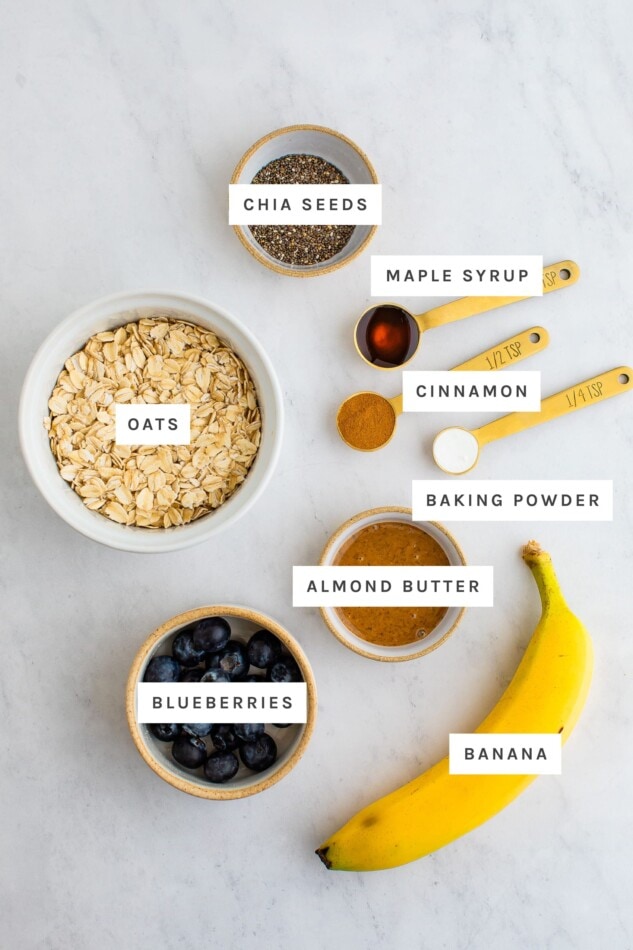 Ingredients measured out to make an oatmeal breakfast cookie, chia seeds, maple syrup, cinnamon, baking powder, oats, almond butter, blueberries and banana.