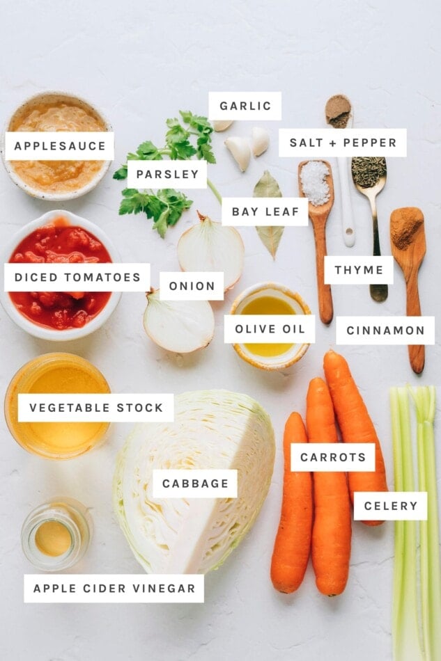 Ingredients measured out to make cabbage soup: applesauce, garlic, salt, pepper, parsley, bay leaf, thyme, diced tomatoes, onion, olive oil, cinnamon, vegetable stock, cabbage, carrots, celery and apple cider vinegar.
