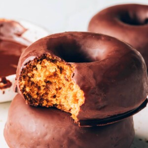 A stack of two donuts. The top donut has a bite taken out of it.