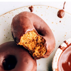 Three donuts on a plate. The first donut has a bite taken out of it.