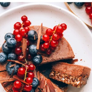 A plated vegan chocolate tart. The tart has been sliced and one of them is on its side so you can see the two layers.