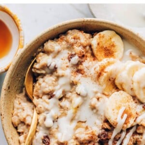 An overhead and closeup photo of a bowl of cinnamon raisin oatmeal topped with banana slices and a drizzle of coconut butter.