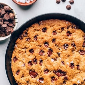 A cast iron skillet containing a baked chocolate chip cookie that encompasses the entire skillet.
