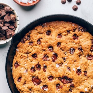 A cast iron skillet containing a baked chocolate chip cookie that encompasses the entire skillet.