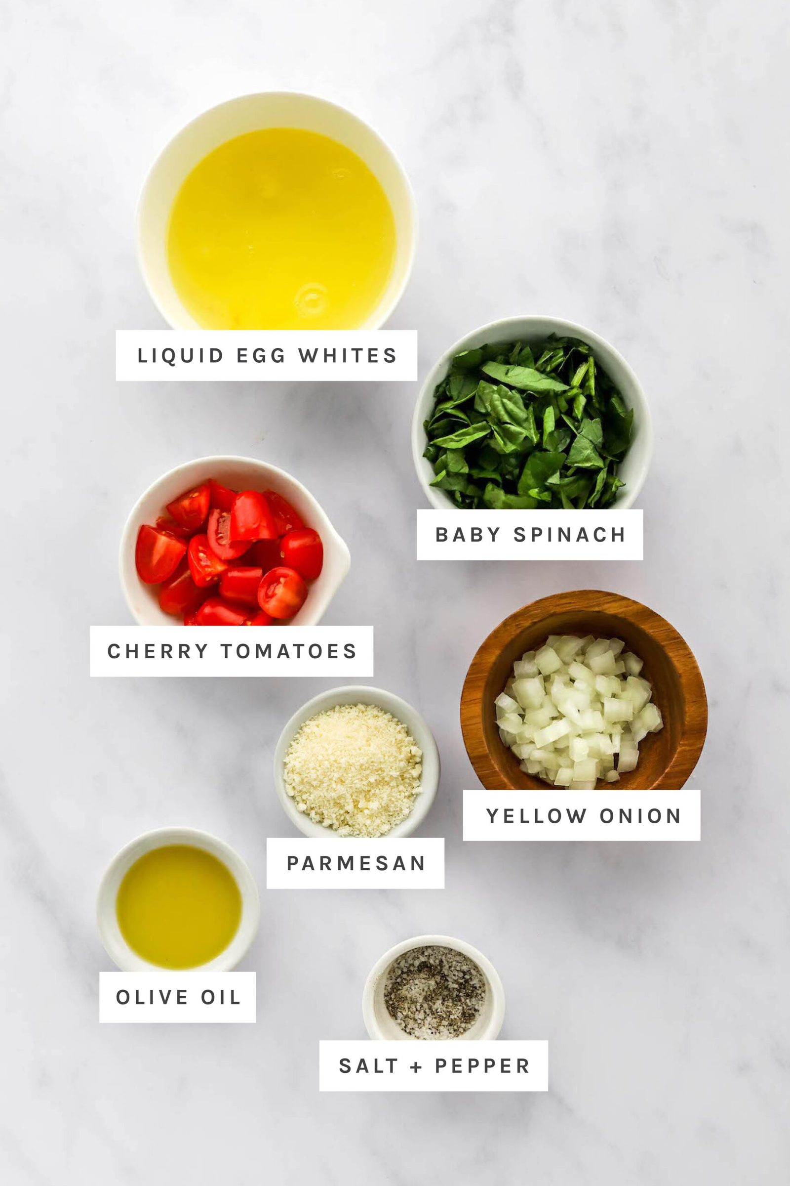 Ingredients measured out to make an egg white omelette: liquid egg whites, baby spinach, cherry tomatoes, yellow onion, parmesan, olive oil, salt and pepper.