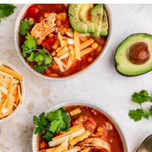 Two bowls of chicken enchilada soup, each topped with shredded cheese, fresh avocado slices and cilantro.