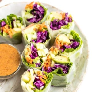 Plate of vegetable spring fresh rolls with chopsticks and a side bowl of peanut dipping sauce.