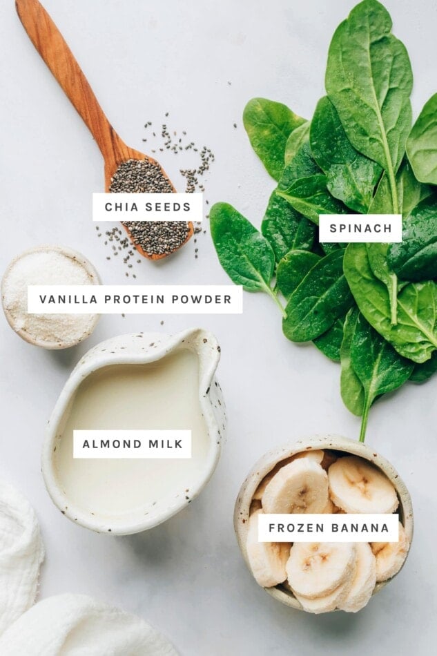 Ingredients measured out to make a green protein smoothie: chia seeds, spinach, vanilla protein powder, almond milk and frozen banana.