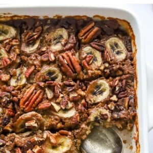 A baking dish containing baked steel cut oats topped with banana slices and pecans. A serving has been removed from the bottom corner.