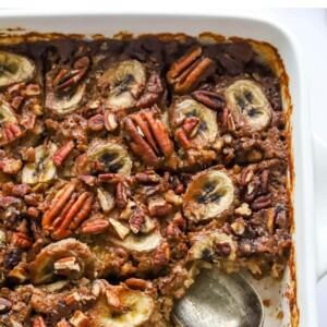 A baking dish containing baked steel cut oats topped with banana slices and pecans. A serving has been removed from the bottom corner.