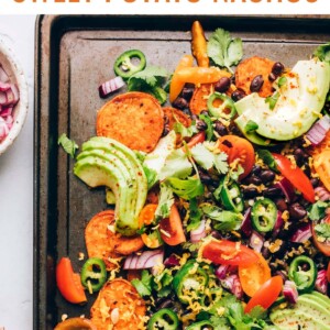 Sweet potato nachos topped with fresh avocado slices, jalapeño slices, and freshly chopped cilantro on a sheet pan.