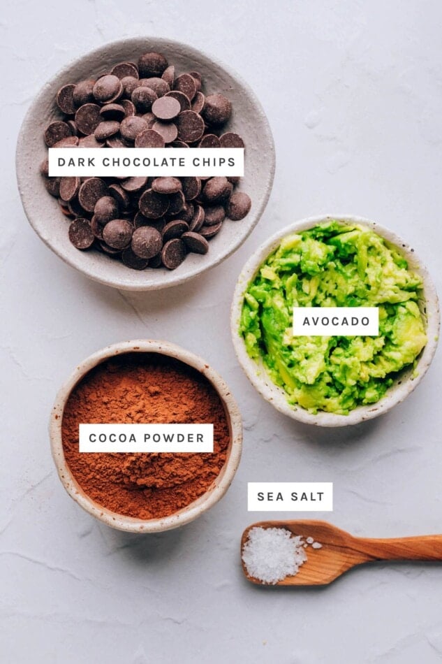 Ingredients measured out to make chocolate avocado truffles: dark chocolate chips, avocado, cocoa powder and sea salt.