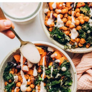 A gold spoon drizzling creamy white bean dressing on top of a vegan power bowl.