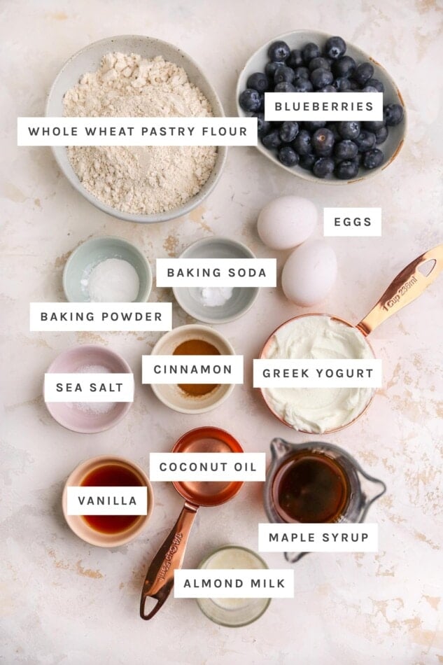 Ingredients measured out to make yogurt muffins: whole wheat pastry flour, blueberries, eggs, baking soda, baking powder, cinnamon, sea salt, greek yogurt, vanilla, coconut oil, maple syrup, almond milk.