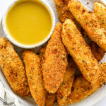 An overhead view of a plate holding air fryer chicken tenders. There is a bowl of honey mustard dipping sauce on the plate with the tenders.